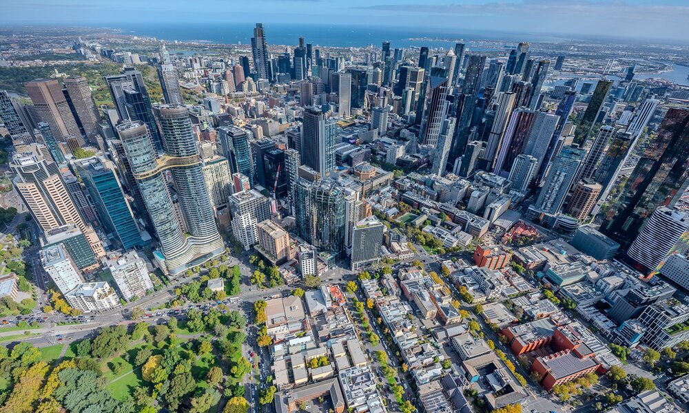 An aerial view of a city with a park, skyscrapers and ocean.