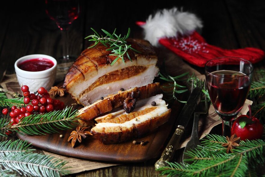 Slices of stuffed turkey roll on a wooden platter surrounded by holly, Santa hat and glass of wine.