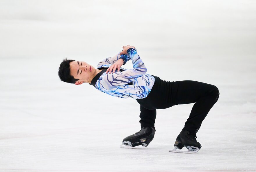 An ice skater bent far backwards while skating  at a rink. 