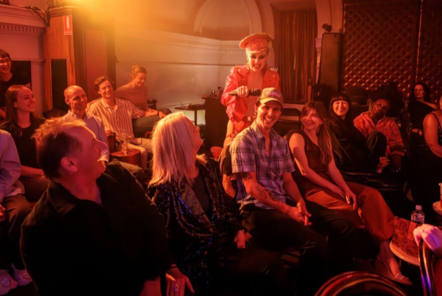 A performer interacting with the seated audience in a small cabaret venue.