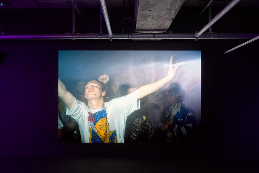 A darkened room where a projection of a person dancing at a rave is playing. 