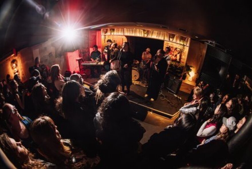 Fish-eye lens view of a mall venue with musicians on a small stage surrounded by audience.