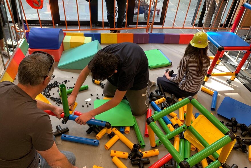 Kids sitting on the floor building with play construction equipment.