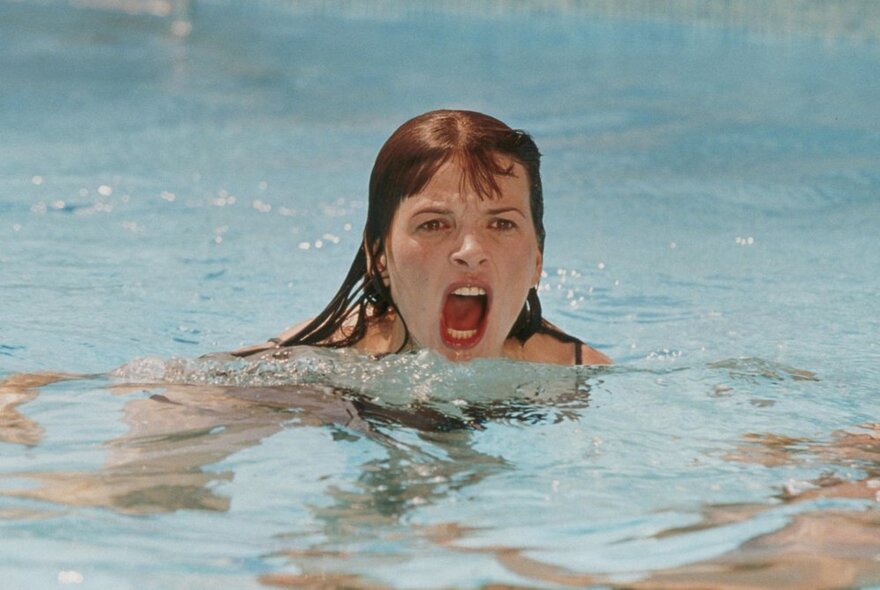 A still image from a film of a woman yelling in a swimming pool. 