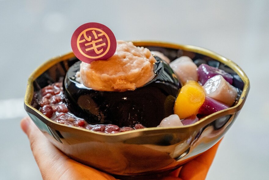 A hand holding a bowl of taro dessert with a branded token on top.