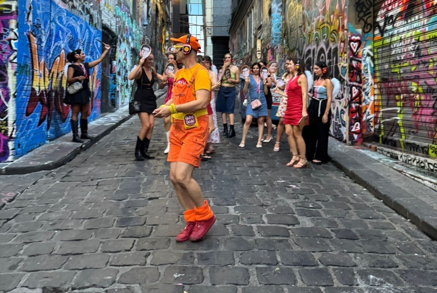 Silent disco group in a city laneway let by a man dressed in orange. 