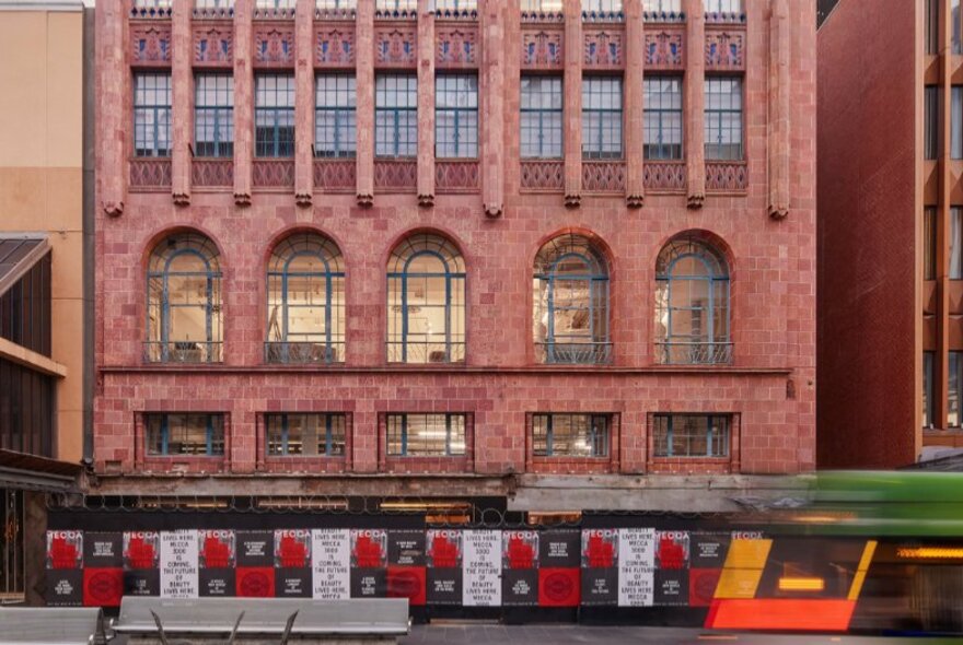 Exterior of a Gothic style building in Melbourne's Bourke Street, with hoardings at street level.