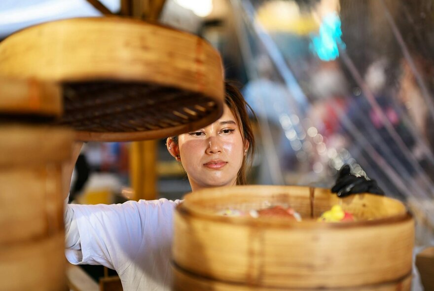 A woman taking the top layer off a bamboo steamer.