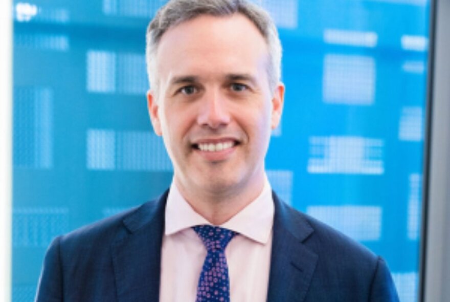 Portrait of a man in a blue suit and tie, in front of a blue and white digital-looking background.