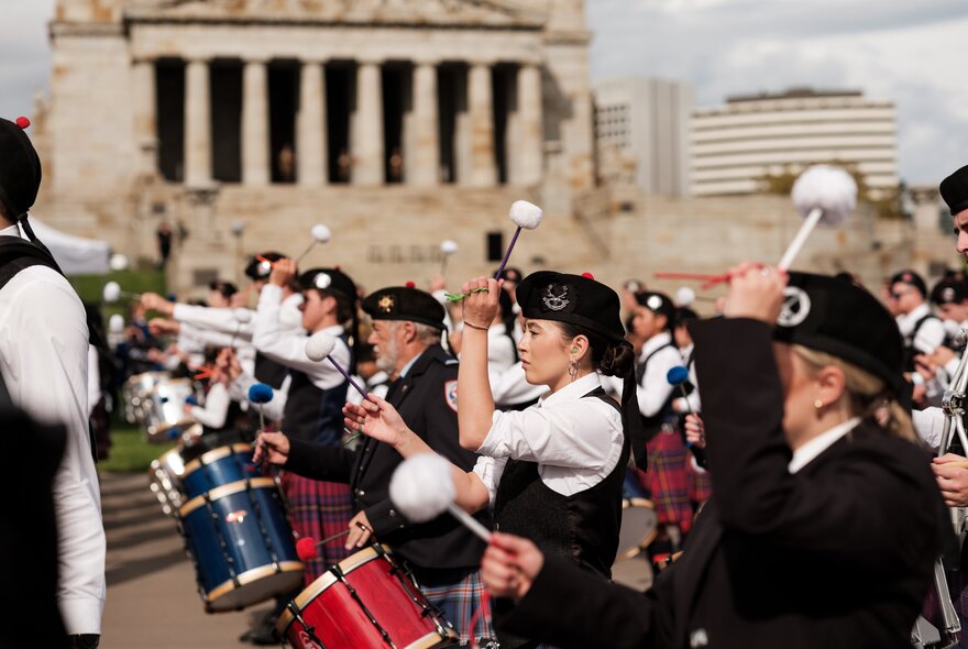 A marching band in kilts, marching and playing in front of the Shrine of Remembrance.