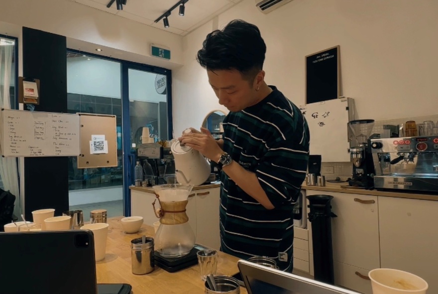 Barista pouring water into a coffee jug in an industrial kitchen.