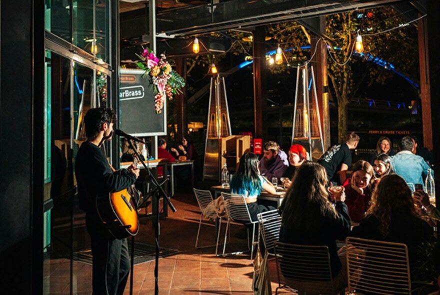 Performer playing a guitar to restaurant diners in a dark interior.