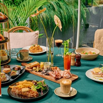 Table set with food and drinks next to potted palms.