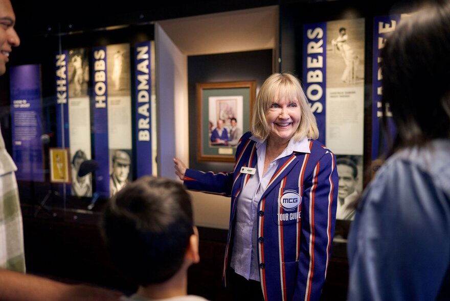 A tour guide in a striped blazer pointing at information on a wall for a tour group.