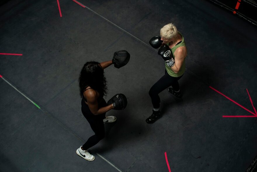 Aerial view of two people wearing black boxing gloves and sparring inside a boxing ring.