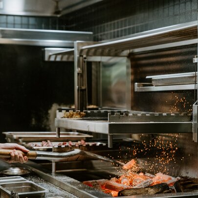 A chef stoking coals with a spade in a commercial kitchen, sparks flying. 