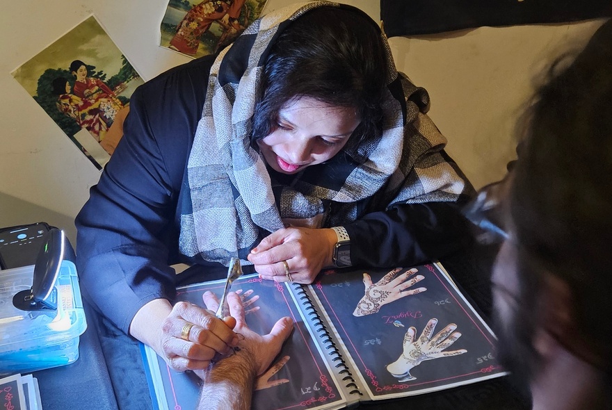 A person applying henna tattoos on the back of someone else's hand.