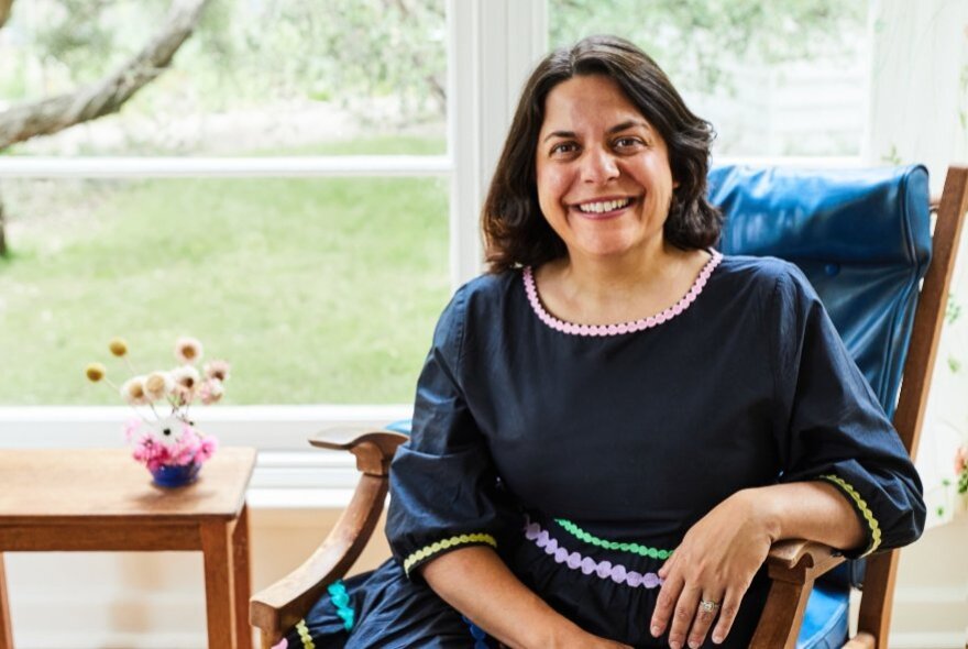 Jaclyn Crupi, seated in a chair by a window looking onto parkland.