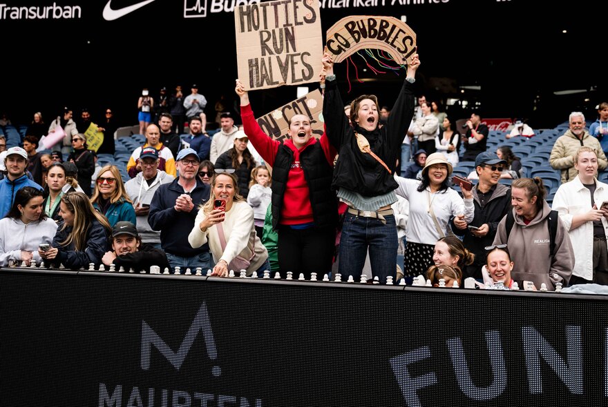 Spectators at the Melbourne Marathon Festival finish area, holding signs in support of the runners.