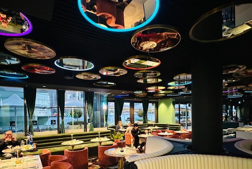 Interior of 30ml Bar and Eatery, with patrons seated at round tables, large windows looking out onto the Esplanade, and round mirrors on the ceiling reflecting the tables below.