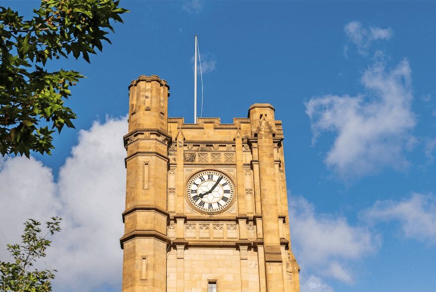 The historic Old Arts clock tower at the University of Melbourne set against a blue sky.