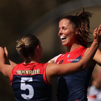 Two Melbourne AFLW players celebrating on the field, coming together for a hug.
