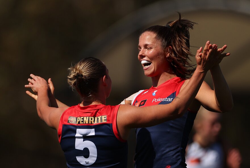 Two Melbourne AFLW players celebrating on the field, coming together for a hug.