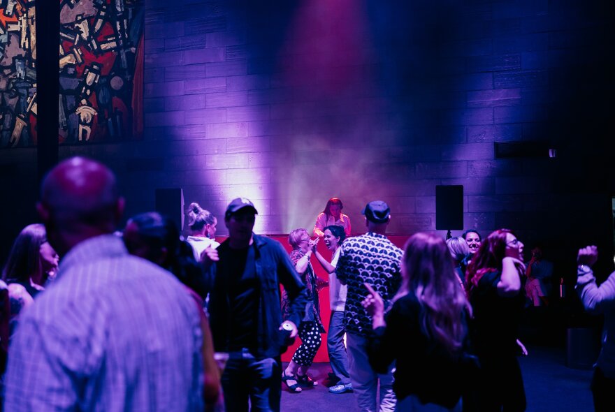 A performer with a standing audience looking on in the NGV, stained glass visible and purple lighting. 