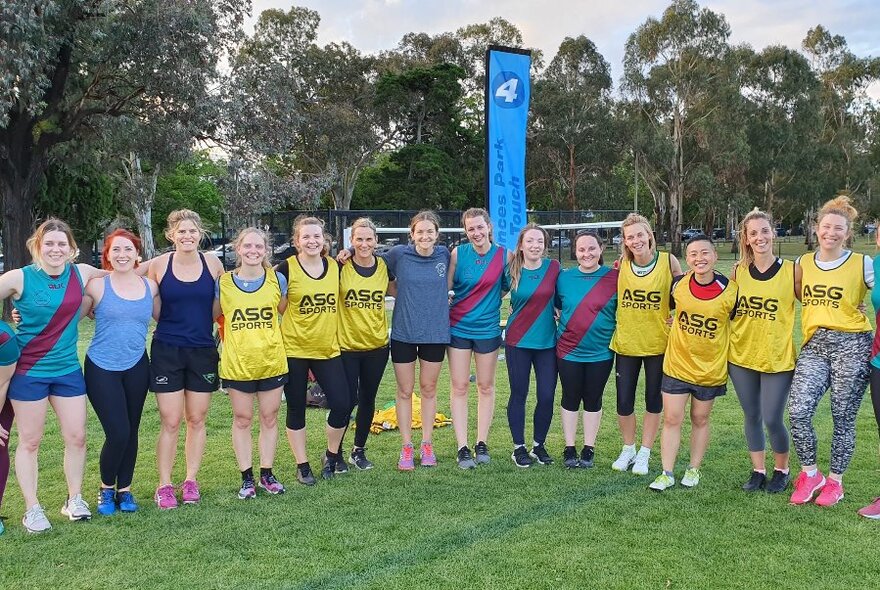 Team of women standing arm in arm on a sporting field with trees in the background.
