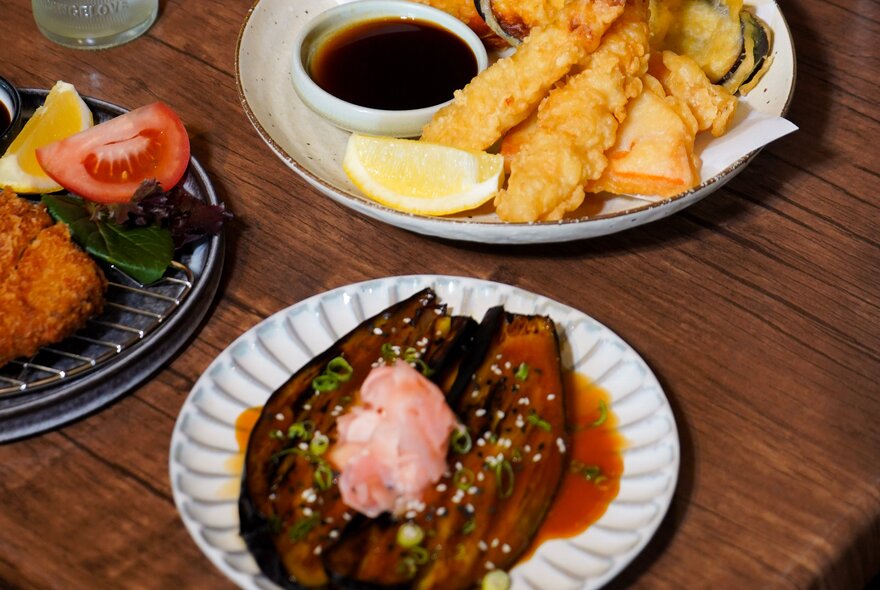 A Japanese dish of agedashi eggplant next to tempura prawns on a wooden table.