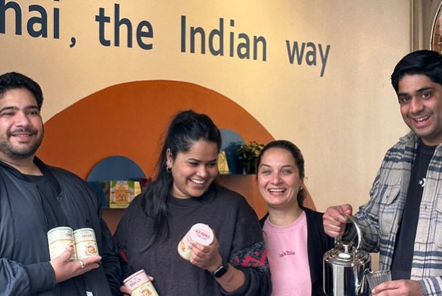 Smiling staff holding containers of chai and pouring tea inside a shop at Queen Victoria Market.