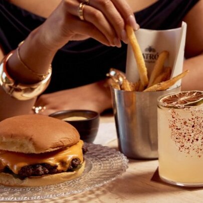 A woman with a burger, fries and spicy cocktail. 