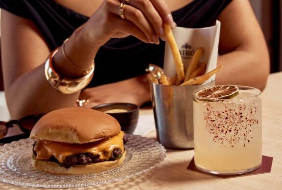 A woman with a burger, fries and spicy cocktail. 