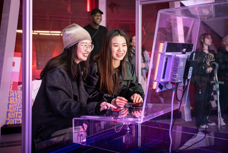 People playing with an interactive exhibit in a neon-lit gallery space.