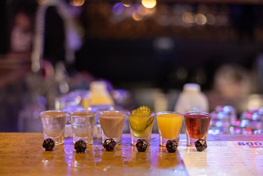 A line of six different coloured shots lined up on a bar. 