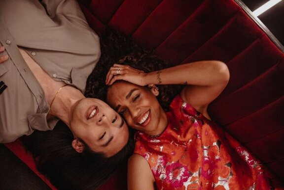 Overhead view of two people who are lying cheek to cheek on a couch and smiling.