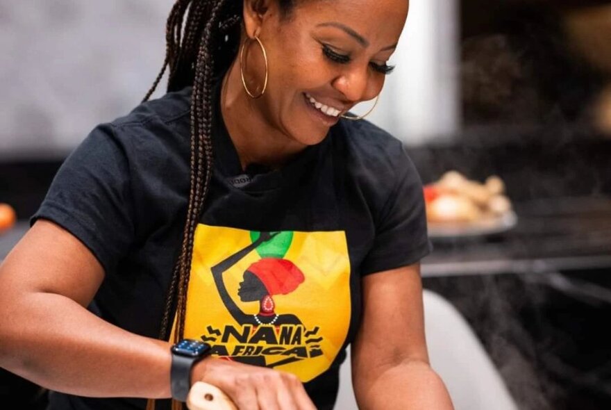 An African woman wearing a Nana Africa t-shirt, smiling as she looks down.