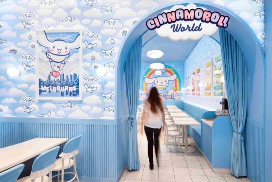 The light blue cloud-covered entrance to a blue shopfront; a woman walking into the store.