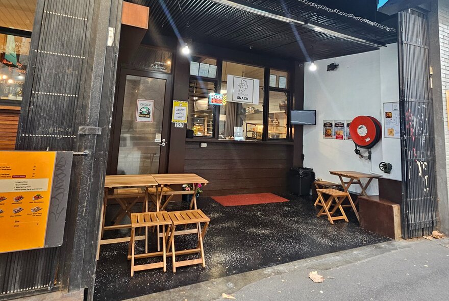 Small outside dining area with tables in front of cafe door and window on street.