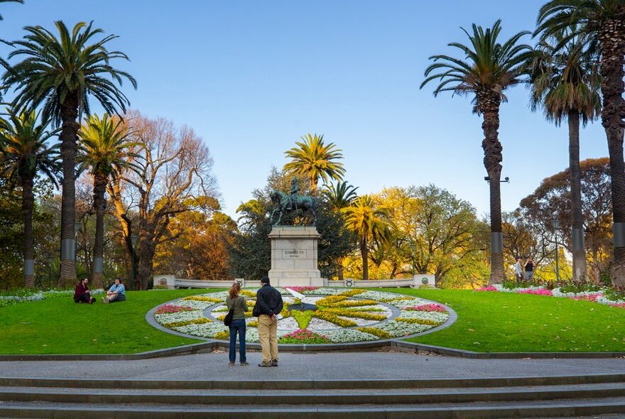 Two people looking at a giant flower garden shaped like a clock.