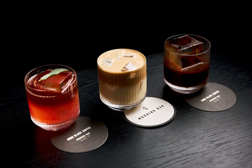 Three glasses of iced coffee lined up on a black counter with placemats.