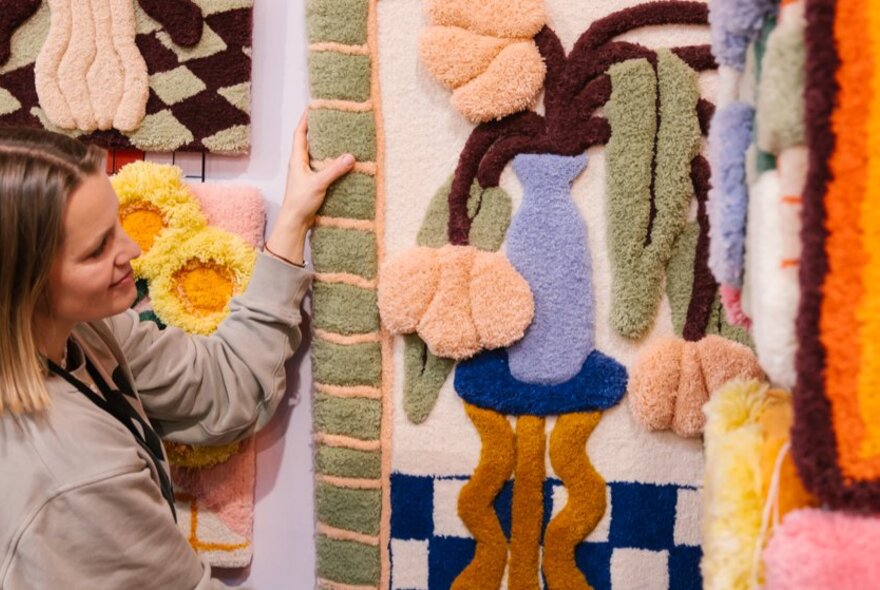 A shopper examining a large colourful wall rug hanging up on display at a design market.