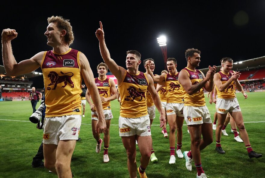 Brisbane Lions players looking triumphant and walking off a football field. 