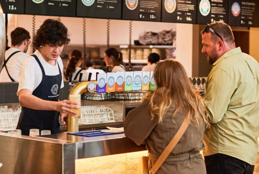 Two people ordering drinks at the bar from a bartender at St Andrews Beach Brewery at Melbourne Park.
