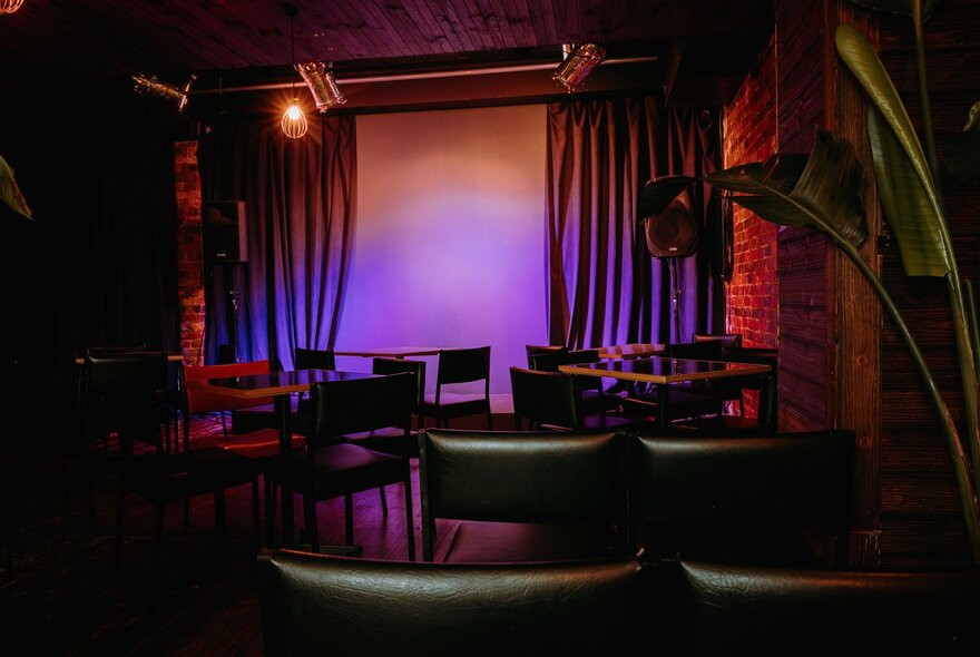 A lit up but empty stage, seen from behind rows of empty chairs in a theatre setting.