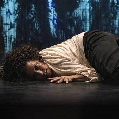 Performer lying on the ground with hands outstretched, blue patterned fabric in the background.