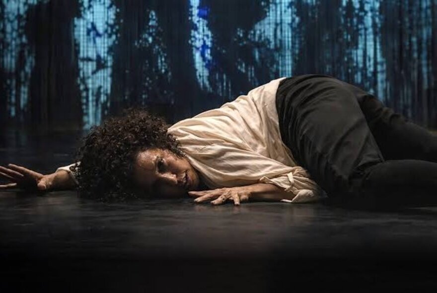 Performer lying on the ground with hands outstretched, blue patterned fabric in the background.