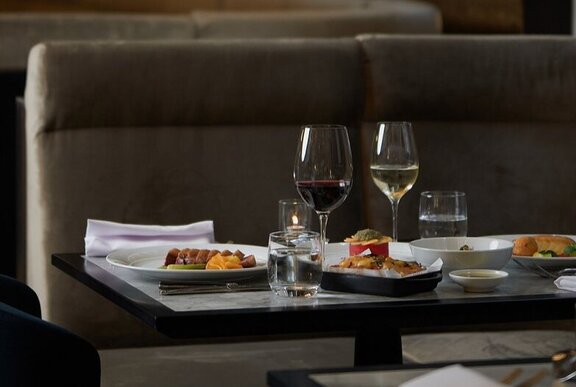 A dining table in a restaurant with dishes of food, white cloth napkins and glasses of wine.