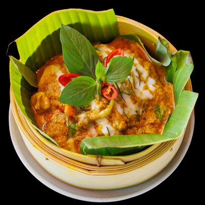 Looking down at a banana leaf lined bamboo steamer containing Cambodian food with Thai basil and chilli garnish. 