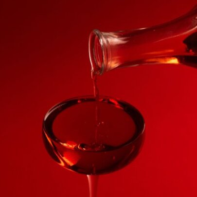 Red cocktail being poured from red bottle into red glass.
